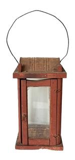 M320 Pennsylvania wooden Lantern featuring four glass panels contained within a wooden post construction frame retaining an old red painted surface. Tiny wire loop hinges allow the door to open freely for access to the interior. There is a hole in the top for ventilation purposes and the make-do hood that protects the internal flame from wind/rain is created with part of an old metal can. A wire bail handle is attached to the top for carrying/hanging purposes. Measurement: 5 ½ square x 10 ¼ tall at corner posts. Overall height is approximately 15 ½ tall including handle in upright position.