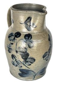**SOLD** K271 19th century Baltimore, Maryland Peter Herman one gallon Crock Pitcher stamped I. There is a small hairline crack in the rim. This small stoneware pitcher was made in Baltimore circa 1850 to 1870. It is decorated in cobalt with a two-stemmed flowering plant, along with flowers on the rim and highlights at the handle terminals. Measurements: 10 ¼ tall.