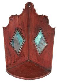 **SOLD** RM1626 Mid-19th century Pennsylvania hanging corner candle shelf retaining its original red painted surface. Shelf features two diamond shaped mirror inserts to reflect the candlelight and a decorative cut out top with hole for hanging. Tiny square head and wire nail construction. Circa 1850s. Measurements: 8 ½ deep x 17" tall. Each of the diamond shaped areas measures 7 ½ wide x 5 ½ tall.