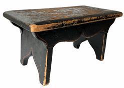 J152 Pennsylvania paint decorated wooden foot stool retaining original black painted surface with remnants of floral paint decoration on the top and simple pinstriping accents on the apron and each of the slightly splayed legs. The drop aprons on each side are mortised into the legs and boast a nice cut out that matches the cut out on each leg/foot. Chamfered edges along the top show extensive wear indicative of years of use. Square head nail construction. Circa 1840-1850s. Measurements: 15 ¾ wide x 8 ¼ deep x 8 tall