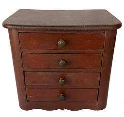 F105 Late 19th century miniature four drawer Chest in the original red paint. The top is one board with panel sides, a nice drop apron cut out base. The drawers are nailed construction with original knobs. Measurements: 11" wide x 7" tall x 10" wide