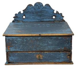 M1111 Early 19th century blue painted wall box with decoratively cut out back, hinged lid and drawer below. The old blue paint is over its original paint decorated surface. Dovetailed case and drawer with both having divided interiors. Small square head nail construction. Circa 1840s. Measurements: 12 ¾ wide x 7 ¾ deep x 6 ½ tall (front) x 14 tall (back).