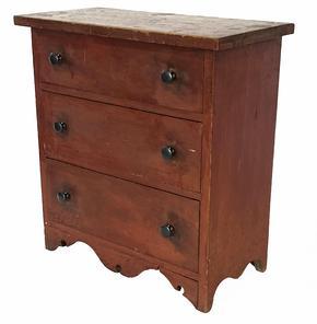 **SOLD** H1000 Excellent late 18th century New England miniature chest of drawers in original red painted surface featuring three graduated sized drawers with chamfered, solid wooden drawer bottoms resting on an exquisite cut out drop front apron and cut out ends. Stretchers are mortised into the front. Small T nail construction. Circa 1790s.   Measurements: 7 5/8" deep x 15 1/2" wide x 16" tall