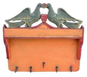 **SOLD** M121 Pennsylvania Folk Art carved and painted hanging rack with original pumpkin, mustard and red painted surface with shaped sides and five (5) forged iron hooks along the bottom edge. The top crest features a cut out Folk Art motif featuring two large carved birds and a heart in original polychrome painted green, red and mustard. The wood is pine with small wire nail construction. Circa 1900-1910. Measurements: 19 3/8 wide x 2 5/8 deep x 18 tall.
