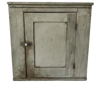 **SOLD** K175 19th century Pennsylvania small hanging corner cupboard bearing original gray painted surface and applied molding along the top. Mortised and pegged door opens to reveal a white painted interior with shelf for added storage. Square head nail construction. The wood is pine. Circa 1860s-1880s. Measurements: 27” tall and takes a 19” corner.