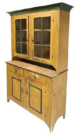 M318 Beautiful mid-19th century Lancaster County, Pennsylvania original mustard and green painted two-piece stepback cupboard boasting an unusual form with a high waisted base (40 ¾ tall). Applied wide cove cornice molding surrounds the top. The upper section has a cut-out pie shelf and two fully mortised 6-pane doors that open to reveal a clean painted interior with shelves and applied plate grooves/stops. The base boasts two dovetailed drawers over two, fully mortised raised panel doors that open to a clean interior with shelves for added storage. Stepback rests on tall cut out feet. The woods are pine and poplar with one-board, square head nail construction. Circa 1850s. Measurements: 61" wide at top (56 ¼ wide at waist) x 20 ½ deep x 87" tall.