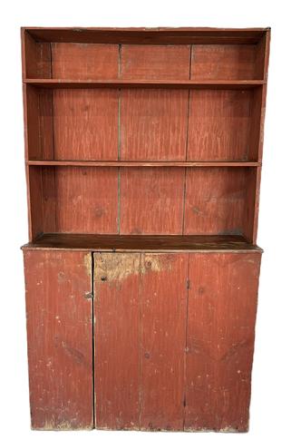 L56 Rare early 19th century New England Cantback Stepback Cupboard bearing original dry, bittersweet red painted surface. Each of the upper shelves bears a carved plate groove and the shelf fronts feature curved ends that cover where they are notched into the sides of the cupboard. The single door below opens to reveal an original blue painted interior. Batton on door boasts large rosehead nails. Circa 1800-1820s. Case is square head and wire nail construction. The wood is pine. Measurements: 43 wide x 17 ¼ deep (at waist) x 72 ¾ tall. 