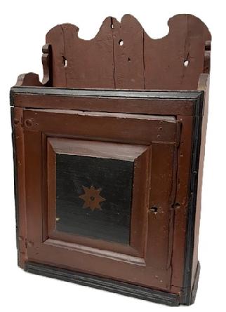**SOLD** L95 18th century Pennsylvania Country Queen Anne painted and decorated hanging cupboard from the collection of Wallace Nutting (1861  1941) retaining original red and black painted surface, shaped sides and backand decorated raised panel door. A circular sticker remains intact on the back that reads Cleaned 10/74. The wood is yellow pine with wooden pegs, rosehead and square head nail construction and original iron hinges. Nice decorative cutout to the back and all front corners are chamfered and molded. Included is the provenance of this hanging cupboard showing it displayed in Mr. Nuttings collection as depicted in Plate no. 516 and 517 of the book: Wallace Nutting Furniture Treasury, Macmillan Publishing Company, Inc. New York, 1928. Measurements: 19 ¼ wide x ~8 deep x 27 ¾ tall (back) x 20 tall (front). 