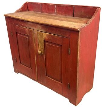 M92 Mid-19th century Pennsylvania Bucket Cupboard featuring two raised panel doors that are fully mortised and pegged retaining old dry, red painted surface. Unusual, shallow depth with solid ends and a clean, natural patina interior. The wood is pine with square head nail construction. All original hardware and knobs. Circa 1820s-1840s. Measurements: 40 wide x 14 ½ deep x 31 tall (front) x 35 tall (back).
