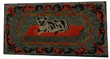 Y217 An outstanding example of American folk art, This hooked rug patterns of the later 19th century, and it was probably hooked sometime around 1890. This rug features a princely Tabby cat on a red rug, A floral garland surrounds the cat, Strips of wool cloth were used for the hooking and it was done on burlap.The rug measures 19 1/2” x 37 3/4”