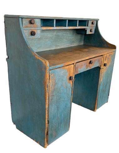 K274 Unusual 19th century Pennsylvania Merchant's Desk with unique hidden hinged drop-down writing surface in old blue painted surface. Desk boasts drawers and pigeonholes in the top section for added storage. The top board is hinged so that it can be raised to utilize the top row pigeonholes for sorting taller items. The lower section, known as a kneehole style, boasts two doors and a center drawer. This versatile piece could be used against a wall or it could be shared by two parties simultaneously as a Partners Desk. Wire nailed construction. Circa 1870s. Measurements: 47 ¼ wide x 20 deep x 41 ¾ tall (back) x 2/ ½ tall (front).