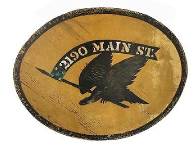 K1834 Double sided wooden sign with an Eagle holding a flag/banner in its beak that reads “2190 Main Street”. Painted in black with polychrome accents on a mustard yellow colored background. Black border detail around the outside edges adds nice appeal. Old eye hooks remain intact on top and wire has been added for hanging purposes. Weathered surfaces indicate years of use in an outdoor setting. Measurements: 21 ½” wide x ¾” thick x 17 ¼” tall.