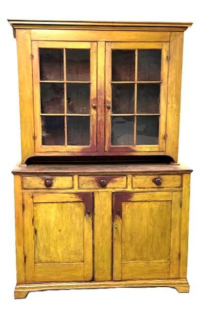L469 Unique early 19th century Lancaster County, Pennsylvania original mustard painted two-piece stepback cupboard boasting an unusual configuration resting on an applied bracket base with cut out feet. The layout of the top consists of two fully mortised and pegged 6-windowlite doors that open to reveal shelves with plate grooves and a spoon rack along the front edge of the middle shelf. The layout of the lower part of the cupboard consists of three drawers over two mortised and pegged panel doors. The base of the cupboard is dovetailed. Nice, deeply beaded edges surround all doors and drawers and also adorn the internal edges of the backboards. The wood is pine with mortised/pegged with �T� nail and square head nail construction. Circa 1820�s. Measurements: 57 &frac14;� wide (at waist) x 20� deep (at waist) x 87� tall. 