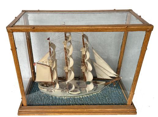 **SOLD** K1639 Late 19th century � early 20th century Ship Diorama in glass case depicting a three-masted ship with full sails flying an American Flag. The highly detailed, unnamed ship is made of what appears to be a salt glazed style pottery with stitched cloth sails and hand painted water. The glass panes (one has a corner crack) are enclosed in a removeable metal case that retains its mustard paint decorated surface. Case Measurements: 20 &frac34;� wide x 10 &frac14;� deep x 16� tall. 