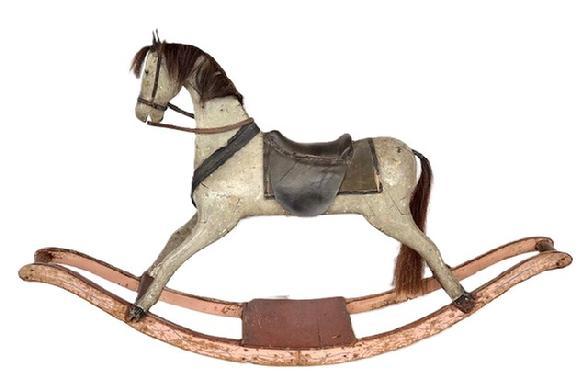 L13 Large 19th century American carved Rocking Horse on bow rockers. The solid wooden carved horse retains its gray painted surface and rests on original salmon painted with blue pinstripe decorated rockers. One rocker has a very early brace that travels along the length of the rocker.  Horse boasts painted eyes, great detailed carved nose/mouth and is adorned with a straw stuffed leather saddle with horsehair mane and tail, realistic metal / leather accoutrements and a saddle blanket. Circa 1850s-1860s. From a Pennsylvania collection. Measurements: 63� long x 12� wide x 37� tall.  