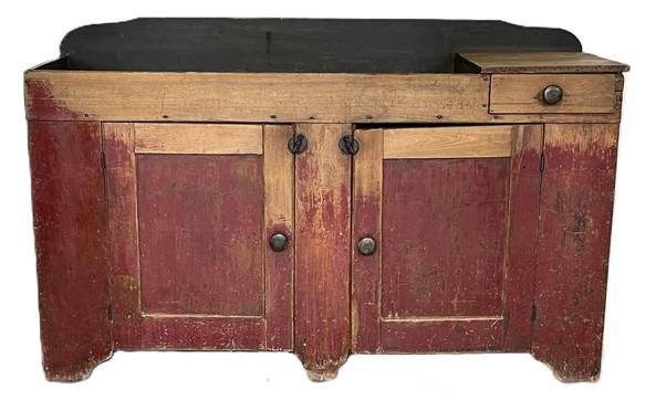 **SOLD** K1723 19th century Pennsylvania original red painted drysink with remnants of blue paint inside the well. One dovetailed drawer. Two doors below the well open to reveal shelf for additional storage. Very unusual long form with center foot to help support the weight. The wood is pine. Great wear on front from years of use. Circa 1850s. Measurements: 60 wide x 21 deep x 35 ¼ tall (back)
